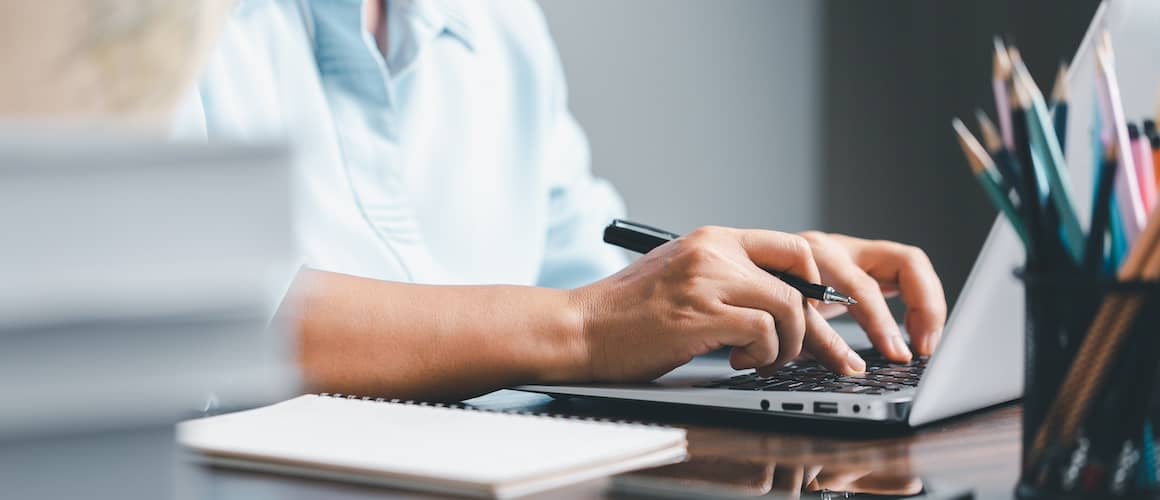 Close up view of a persons hands typing on a laptop's keyboard.