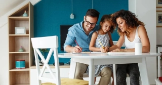 A mom and dad draw with their young daughter at a table together. 