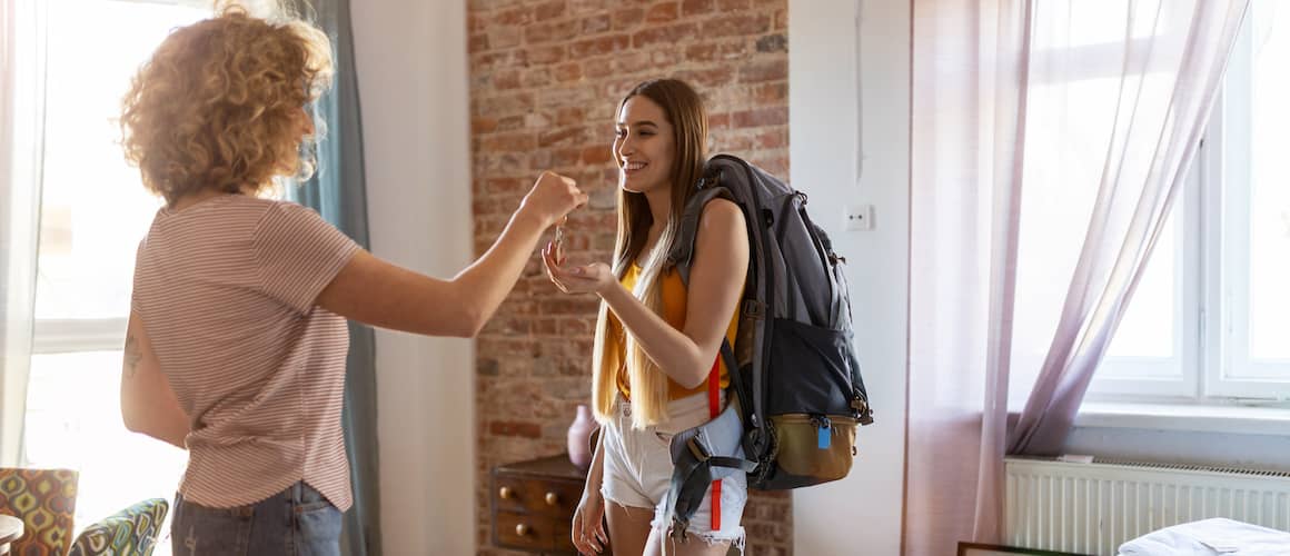 Young backpacker accepts the keys to her new apartment from a woman with curly hair.