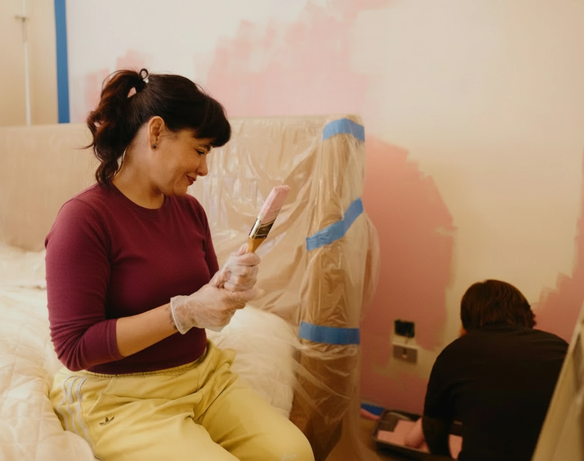 Woman painting a wall while another person paints nearby.