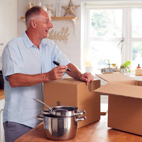 A senior couple packing and labeling boxes in a kitchen, signifying moving or packing activities for relocation.