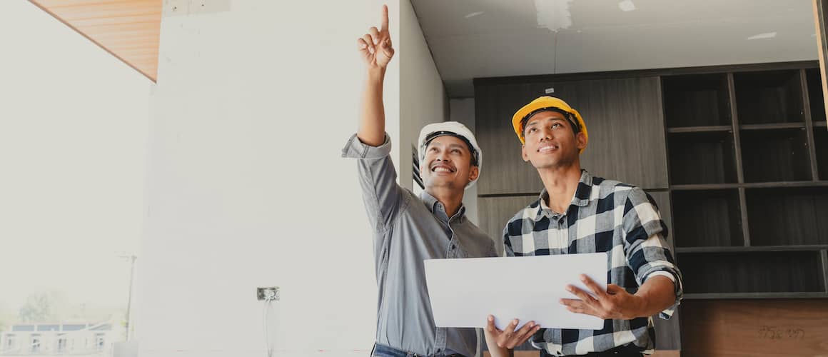 Photograph of contractors holding large house blueprints at a newly built construction site, related to construction or real estate development.