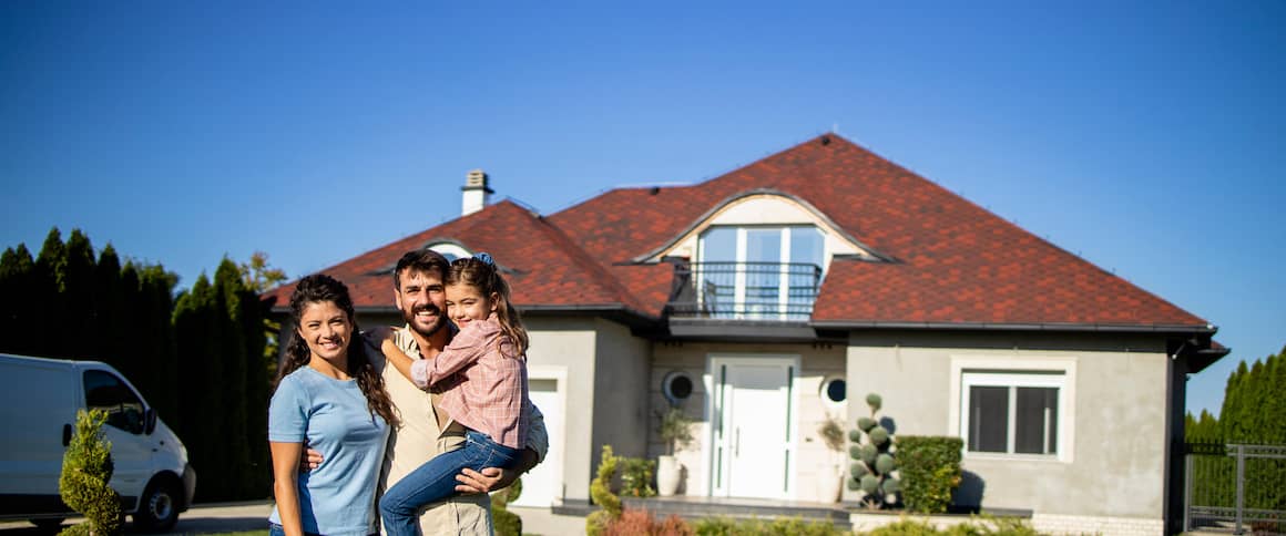 Couple with young daughter standing in front of new home.