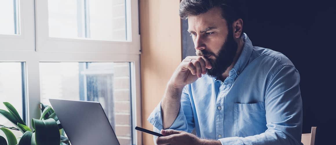 Man in blue shirt sitting at computer thinking.