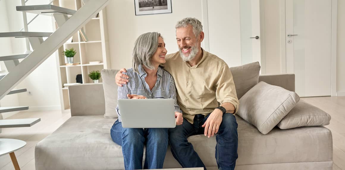 A couple on a couch looking at a laptop, possibly researching or managing their mortgage online.