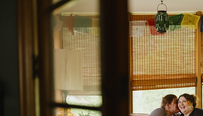 View through inside door of couple sitting out couch smiling.