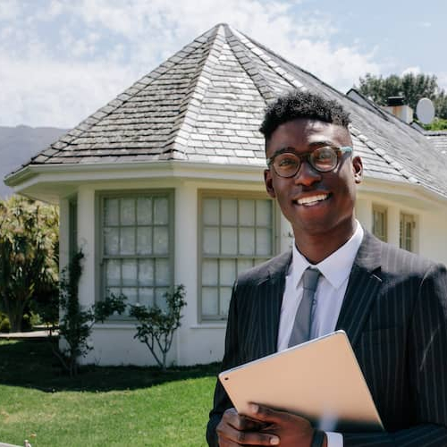 A real estate agent holding an iPad standing in front of a house possibly advertising it for sale.