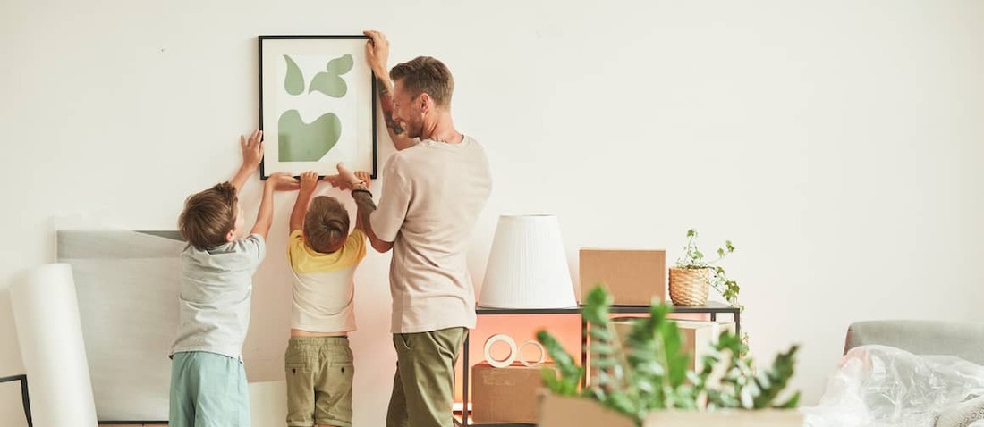 Father hanging painting on wall with the help of his two young sons.