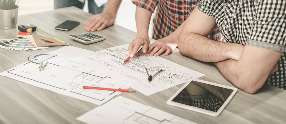 Closeup of blueprints on the table as couple look over them with senior man.