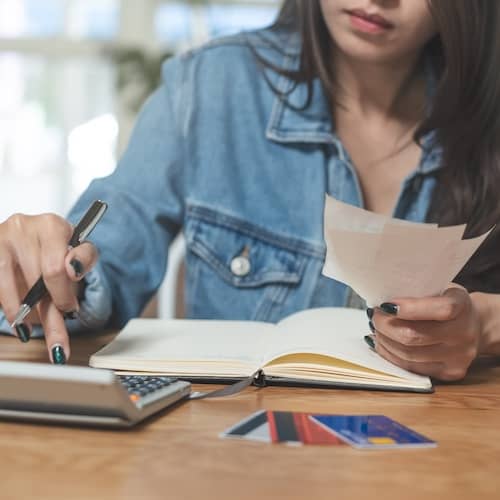 Young woman calculating credit card debt at her kitchen table.