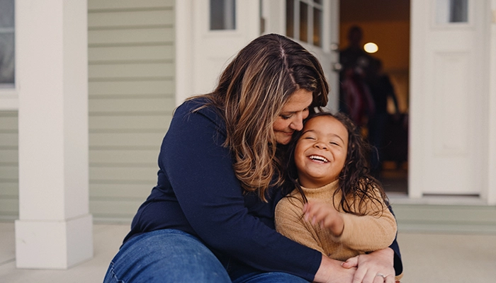 Woman holding daughter while sitting on porch smiling.