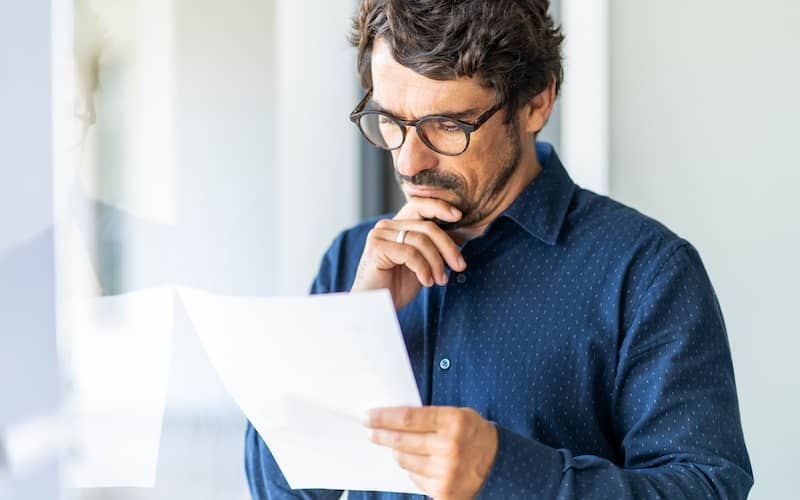 Man in blue shirt with ring reading paper document.