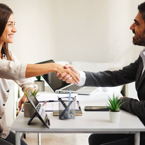 A stock photo portraying a woman shaking hands with a man, potentially in a real estate or home buying context, possibly indicating agreement or partnership.