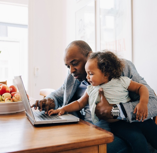 Father sitting at a table with his daughter while he shows her the laptop.