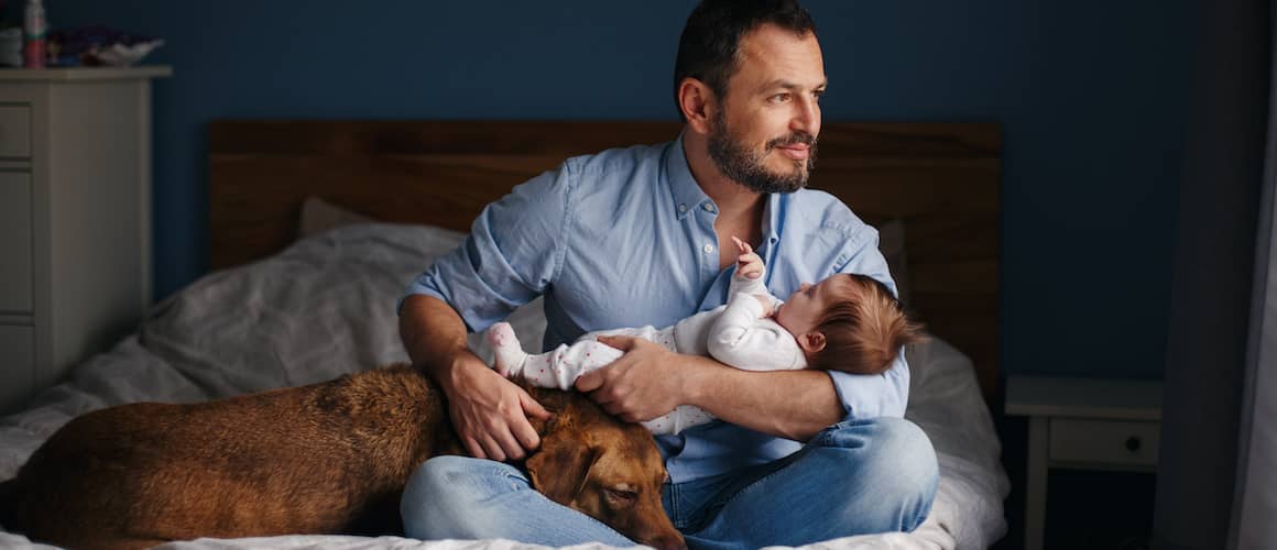 A father holding his child and dog in his lap.