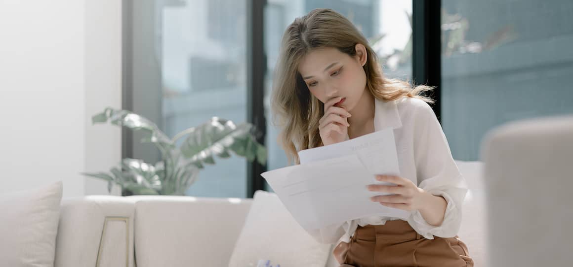 A woman looking worried as she looks over paperwork and bills.