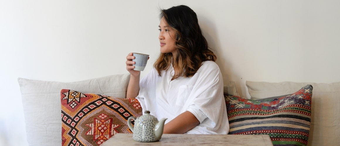 A woman enjoying a cup of tea while sitting on a cozy couch possibly thinking about real estate investment or this choice between renting or buying a house.