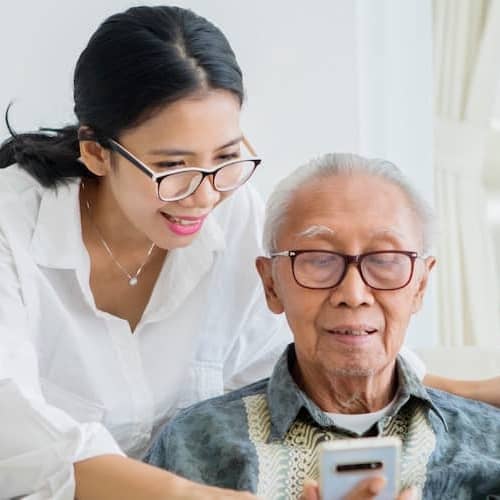 A young Asian woman assisting her father with a phone, possibly related to technology or communication assistance.