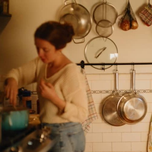 Mother in kitchen cooking while father feeds child in high chair in dining room.