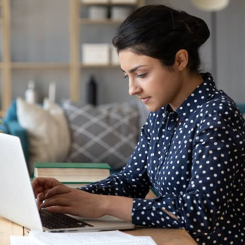 A young woman working on a laptop, possibly in a home or office setting.