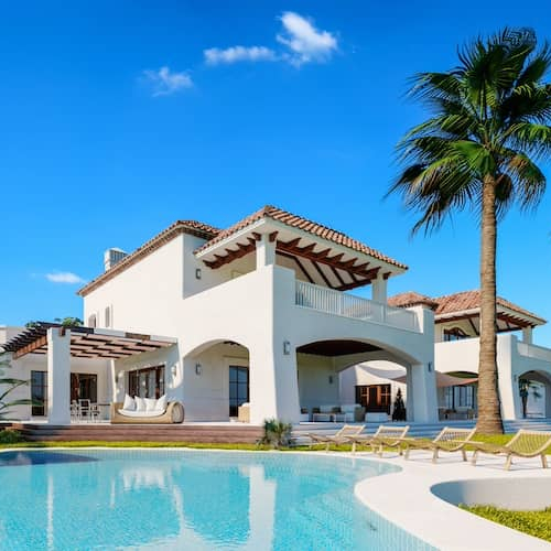 White house with Spanish tile roof, large pool, and palm trees.