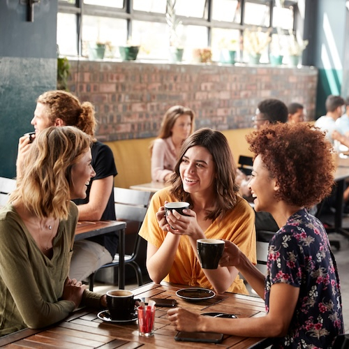 Three young women chatting at cafe.
