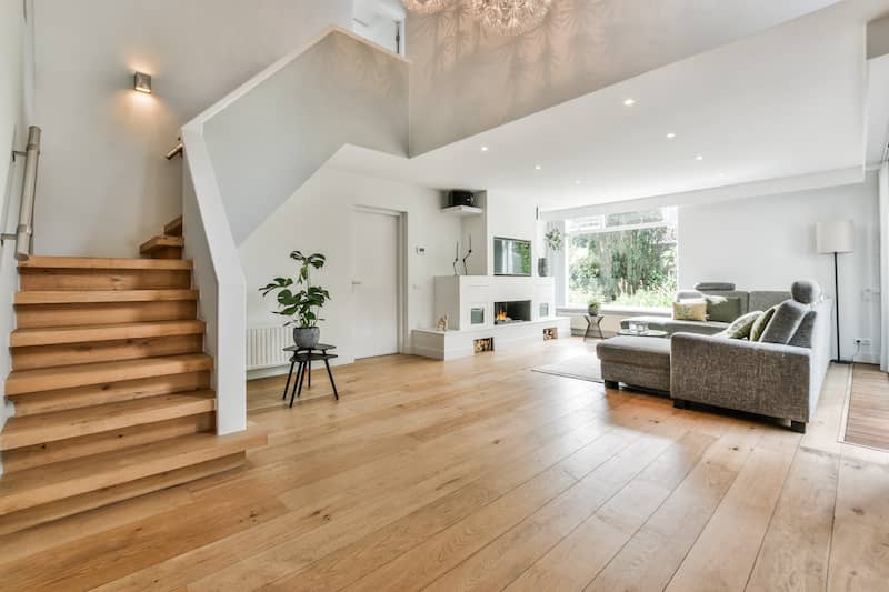 Home interior of a modern home with a wooden floor, large gray sofa and stairs leading to the second floor.