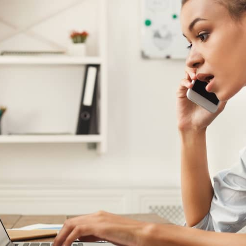 A woman multitasking on a phone call and a laptop maybe discussing a deal.