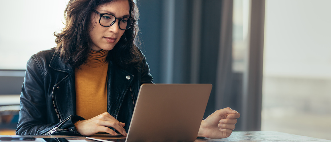 Woman wearing glasses reviewing information on laptop.