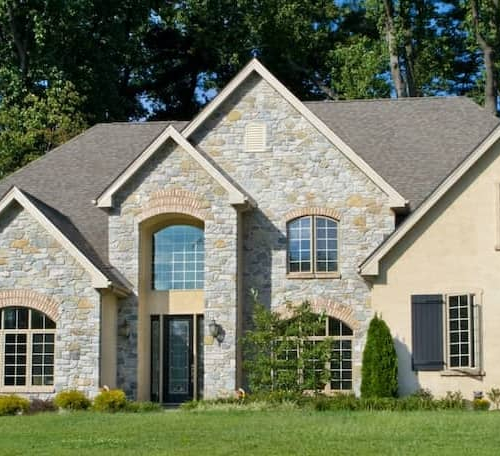 A newly built tan home surrounded by trees, showcasing a newly constructed property.