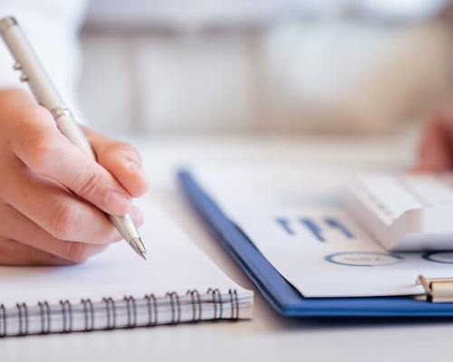 Hands pressing a calculator and writing on a notepad, signifying financial calculations or planning.