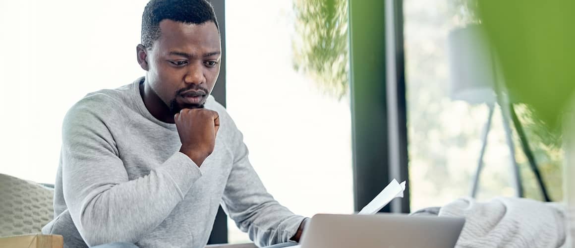 Pensive looking man looking at his laptop at home.