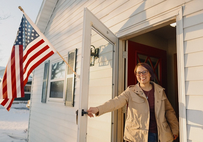 Person opening the front door of a home with an American flag