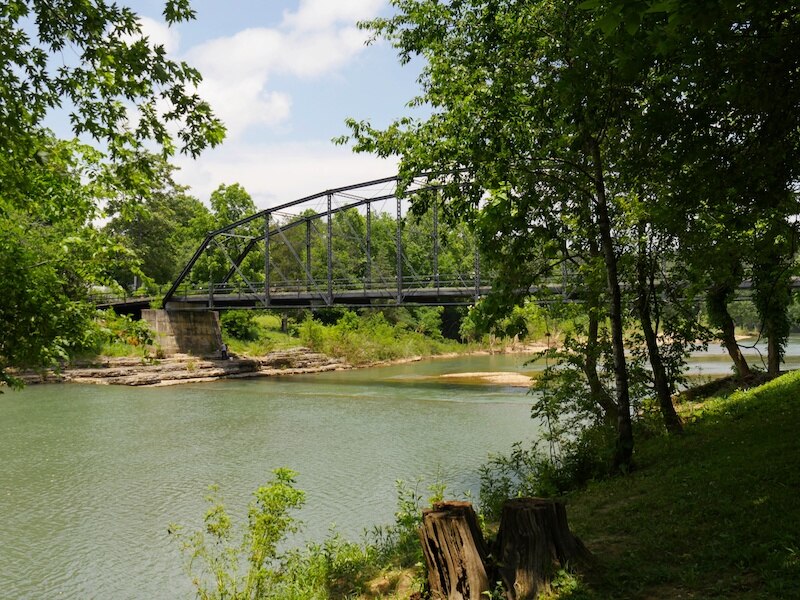 RHB Assets From IGX: War Eagle Mill Bridge in Rogers, Arkansas, surrounded by lush greenery.