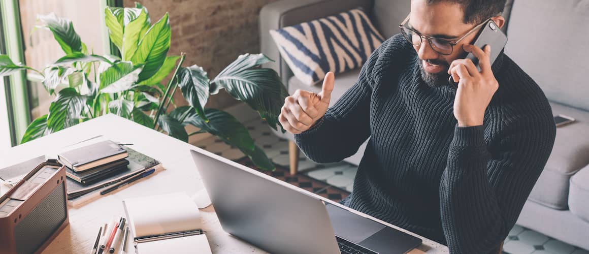 A middle aged man working from home on the laptop and talking on the phone.