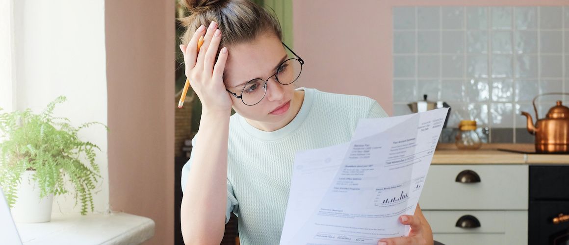 Woman with round glasses holding pencil and looking pensively at a paper in her hand.