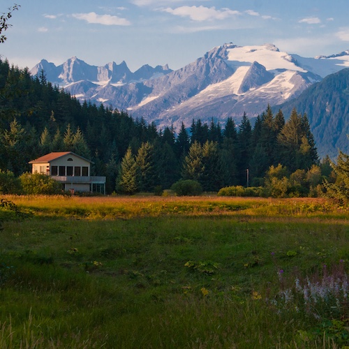 House in field with snow-capped mountains in the background.