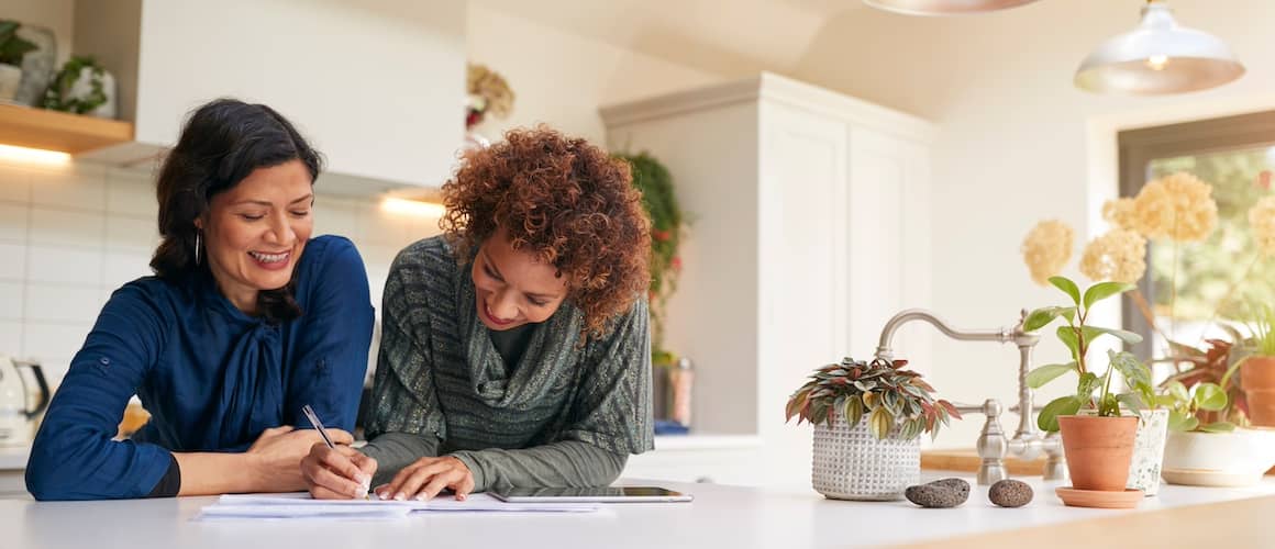 Young, same sex couple standing at the kitchen counter and looking over papers together.