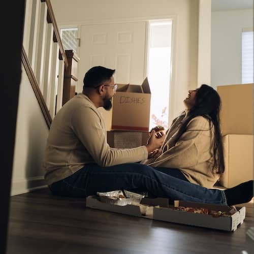 A young couple taking a break from unpacking by sharing a laugh and a piece of pizza.