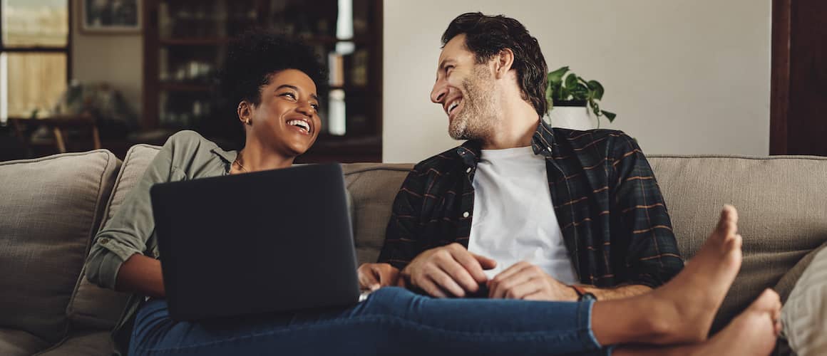 A couple on a couch with a laptop, potentially engaging in real estate-related activities or discussions.