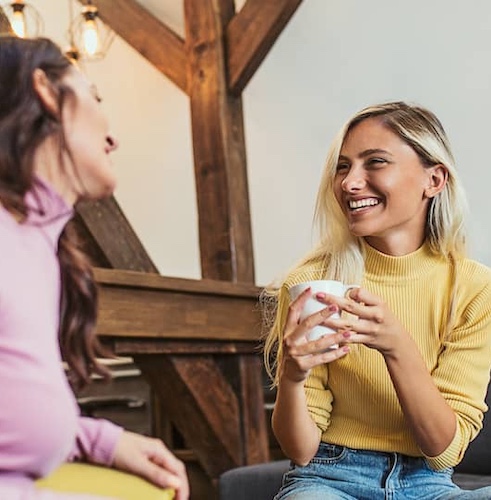 Sisters chatting over coffee in home with exposed wooden beams.