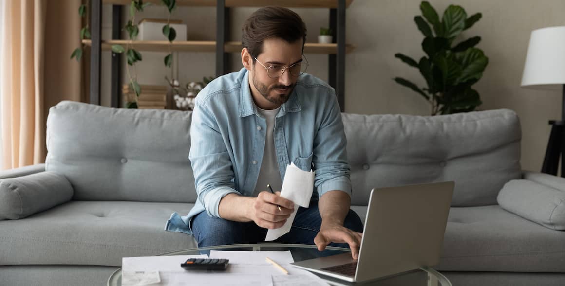 Man sitting on couch working on finances on laptop.