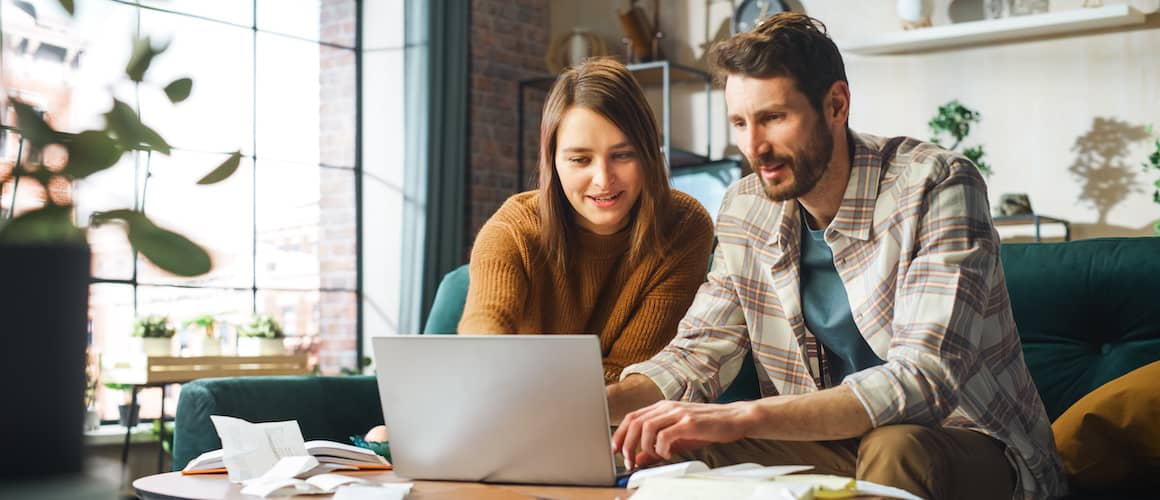 Happy young couple sitting on a sofa together and using a laptop.