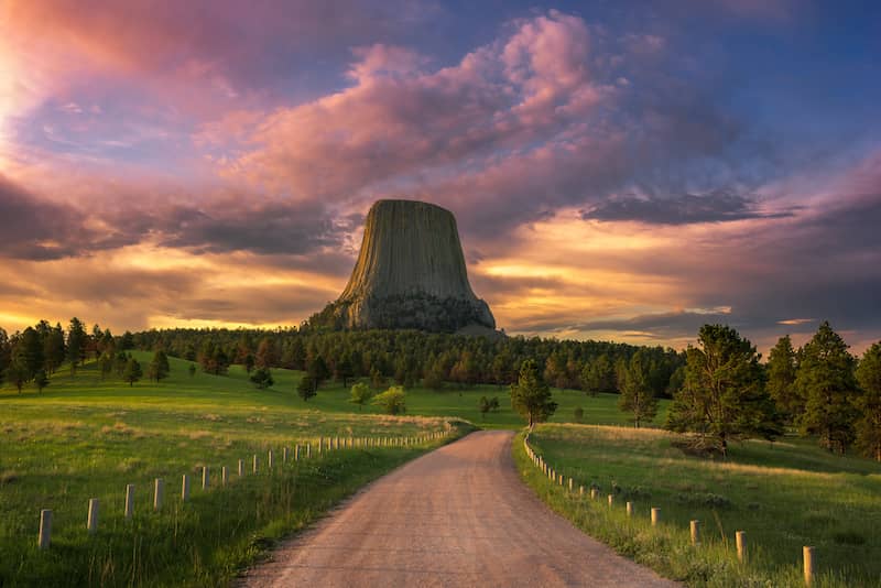 The Devil's Tower landmark in Wyoming, with sunset lit could in the sky beyond.