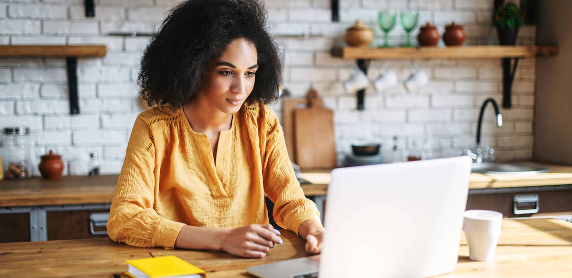 A woman using a laptop in the kitchen, indicating remote work or online activities in a home environment.