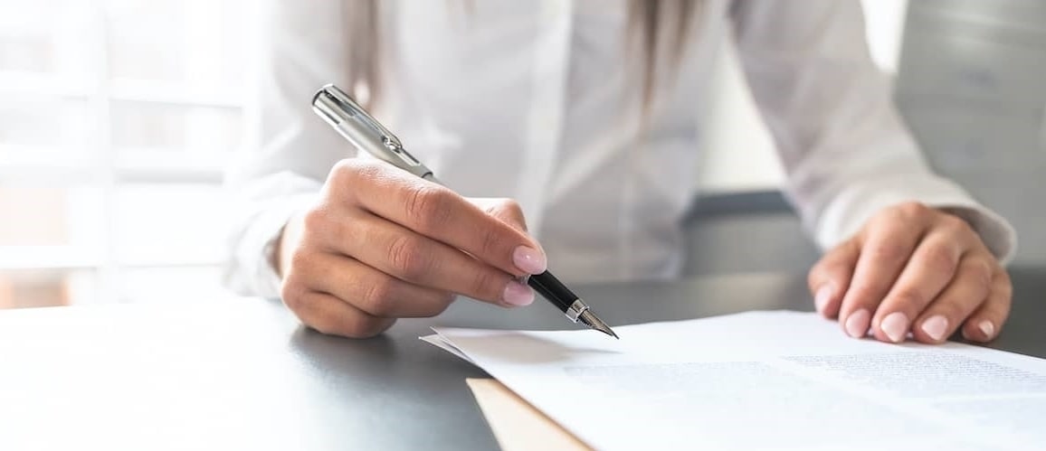 A woman about to sign some documents with a pen.
