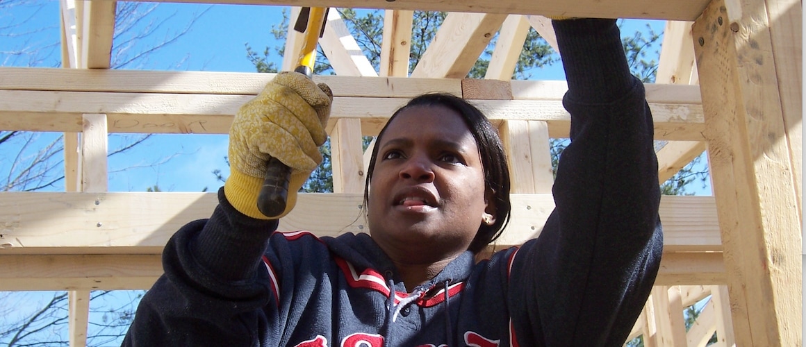 A black woman working on the wooden structure of a new house.
