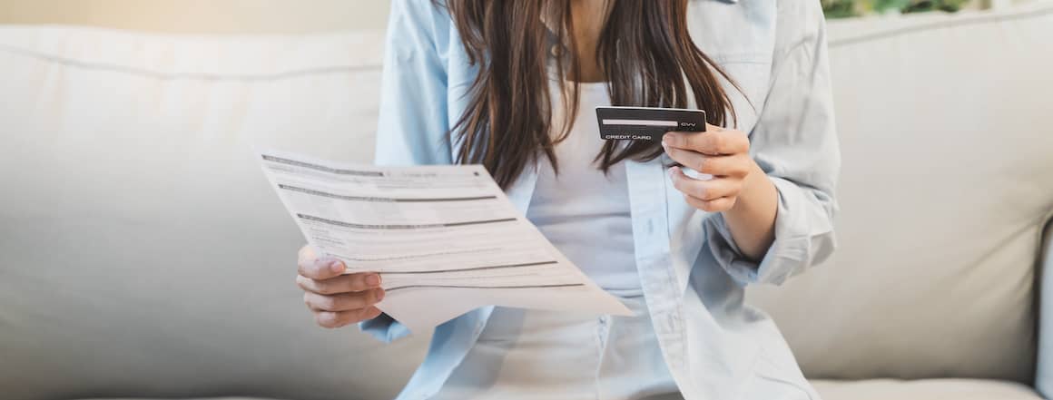 Woman sitting on couch holding a credit card and a document.