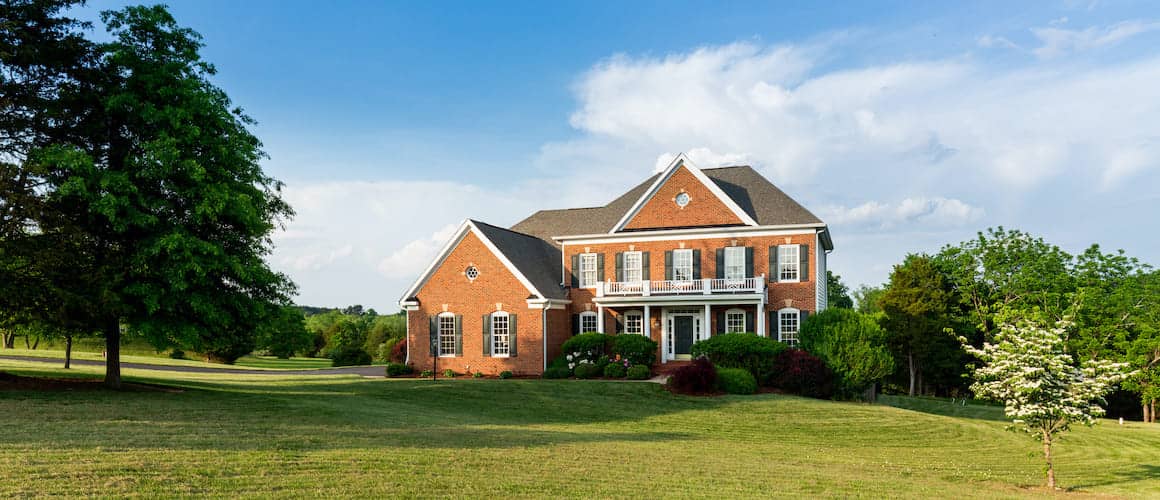 A large brick home with a sprawling green lawn and well-tended landscaping.