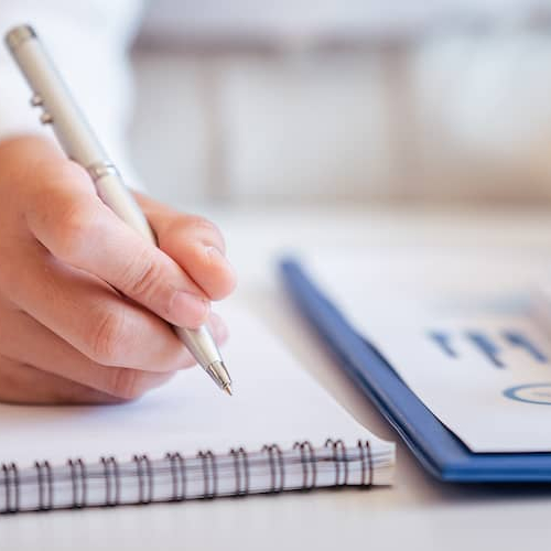 Hands pressing a calculator and writing on a notepad, signifying financial calculations or planning.